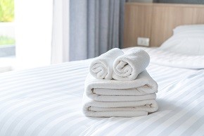 Close up of white fluffy, rolled towels on bed in hotel room for customer.