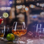 Glass of cognac or whiskey on a bar counter. Assortment of different strong alcohol drinks over night lights background. Copy space
